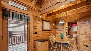 Het interieur van een houten hutje, met een eettafel, stoelen, een kaart en een bord aan de muur.