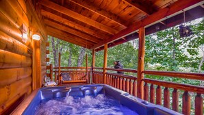 Een houten chalet met een hottub en een terras met uitzicht op een bos.