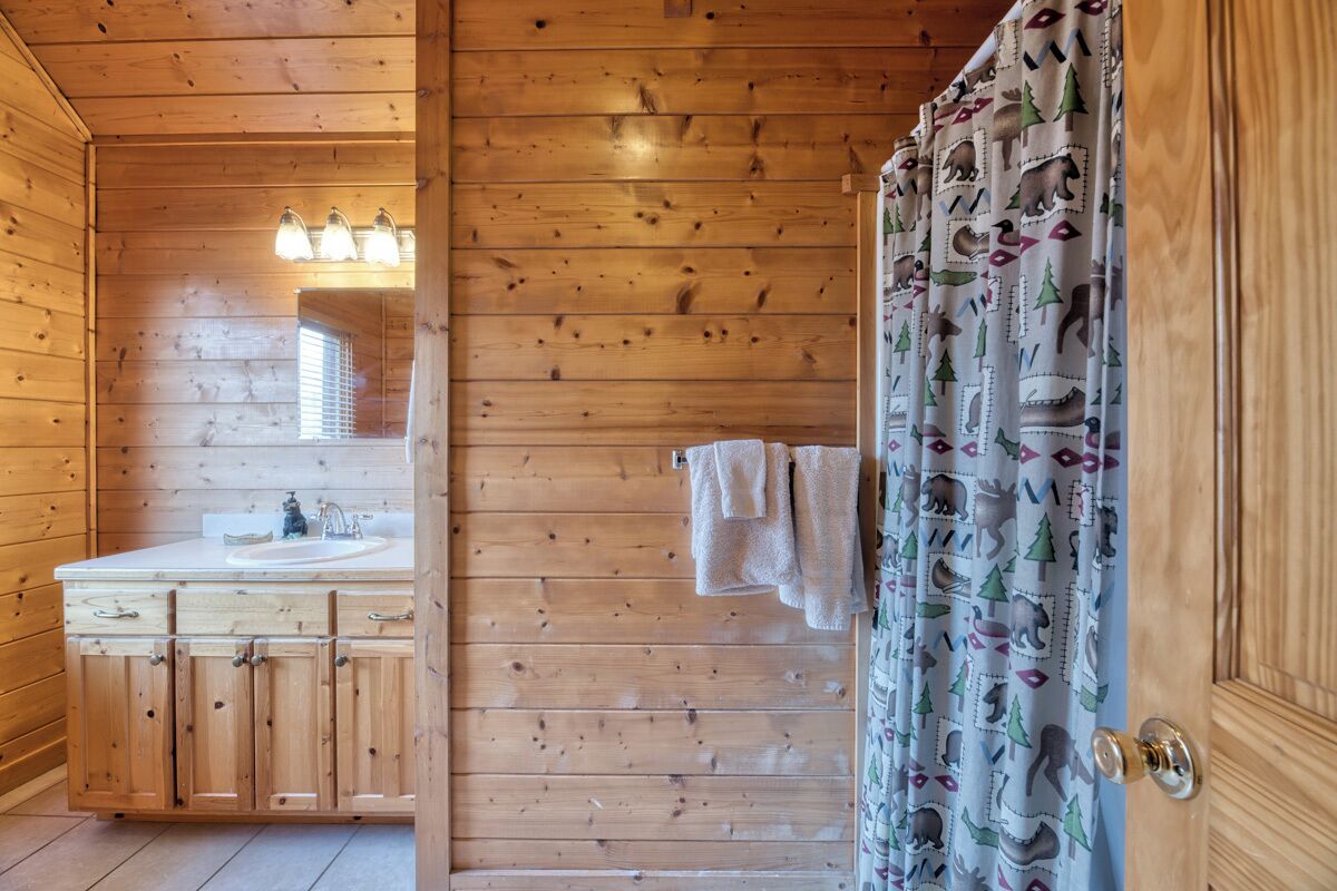 A wooden cabin bathroom with a sink, cabinets, and a shower curtain with animal prints.