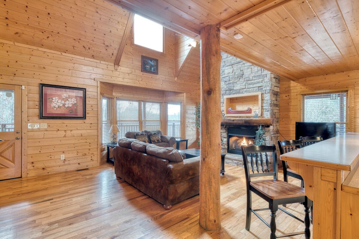 A log cabin interior with a fireplace, wooden furniture, and a stone wall.