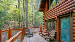Eine Holzterrasse mit Adirondack-Stühlen, einer Glastür und Blick auf einen Wald.