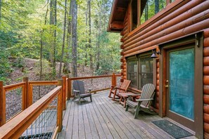 Terraza de madera con sillas Adirondack, una puerta de vidrio y vista a un bosque.