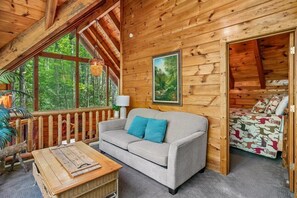 Interior acogedor de una cabaña con sofá, una mesita y ventana con vistas a un bosque.