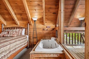 A cabin interior with a wooden ceiling, a bed with striped bedding, a white bathtub, and a ladder.
