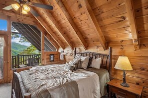 A wooden cabin bedroom with a bed, pillows, a nightstand, and a ceiling fan.