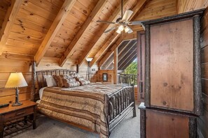 A wooden cabin bedroom with a bed, a nightstand, a lamp, a ceiling fan, and a large window.