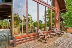 A wooden deck with a glass enclosure, outdoor seating, and a view of the surrounding forest.