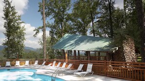 Un espace piscine doté de chaises longues et d’un coin salon abrité, le tout entouré d’arbres et de montagnes.