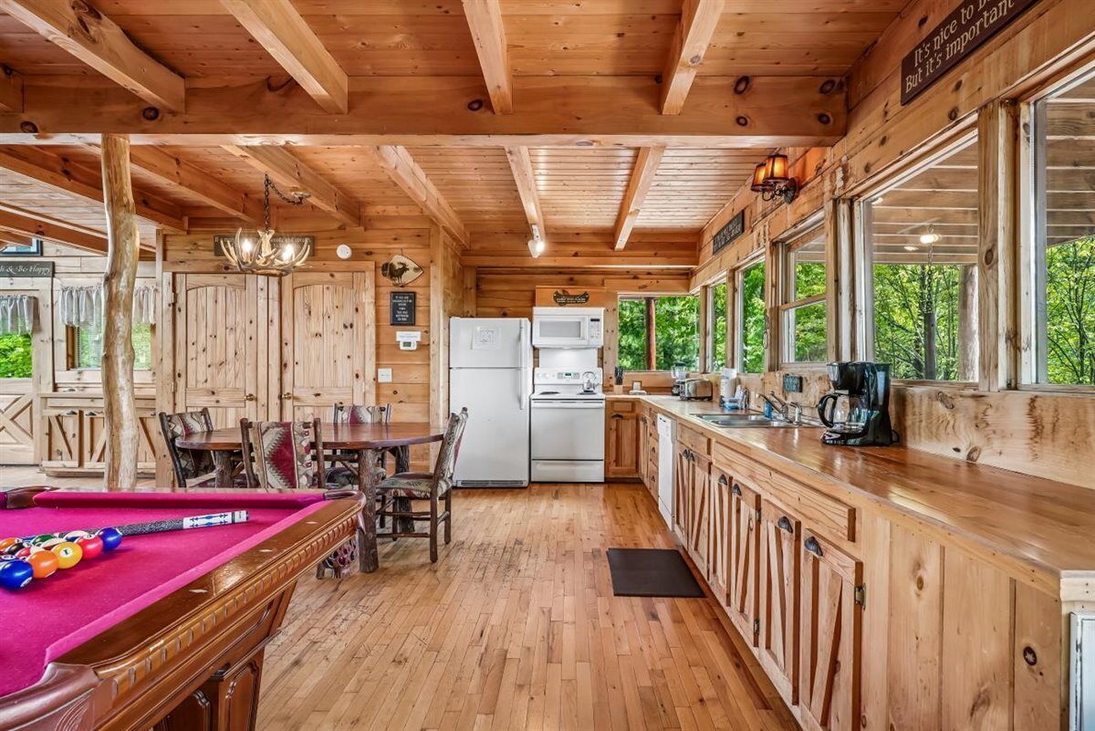 Un intérieur en bois comprenant une table de billard, un coin repas, une cuisine et de grandes fenêtres.