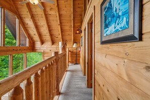 Ein Innenkorridor aus Holz mit Deckenventilator, einem gerahmten Bild an der Wand und Blick auf Grünflächen.