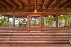 A log cabin interior with a central wooden frame window, wooden logs on the walls, and a ceiling with wooden beams.