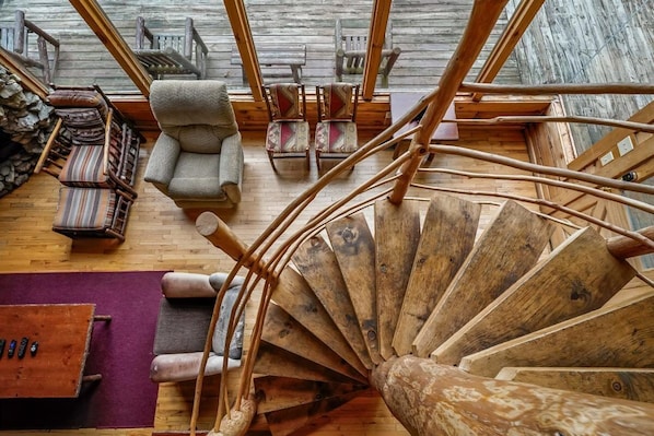 A spiral staircase made of wood, a wooden wall, and a seating area with chairs and a sofa.