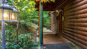 A wooden log cabin with a covered porch, a lantern, and a pathway leading to the entrance. - Rustic Wooded Cabin w/ Game Room & Hot Tub (Sevierville)