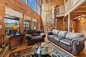 A wooden interior with a staircase, leather sofas, and a glass coffee table.