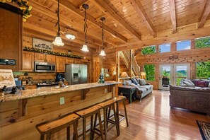 A wooden cabin interior with a kitchen, dining area, and living room. - Rustic Luxe Charm w/ Views, Fireplace & Hot Tub (Sevierville)