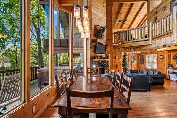 A wooden cabin interior with a dining table, chairs, a sofa, and a TV.