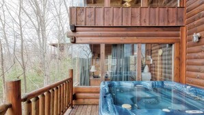 Une cabane en bois avec un jacuzzi sur la terrasse, entourée d’arbres.