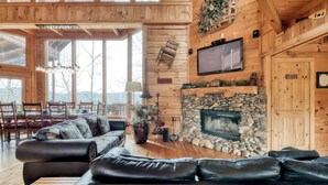 L’intérieur chaleureux d’un chalet avec une cheminée en pierre, des canapés en cuir, un coin repas et un téléviseur fixé au mur.