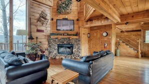 L’intérieur d’un chalet confortable, avec une cheminée en pierre, des canapés en cuir et un escalier en bois.