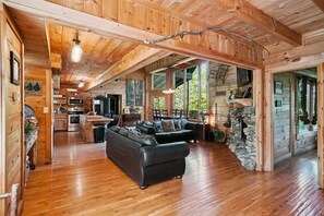 A spacious wooden cabin interior with a living area, kitchen, and stone fireplace.