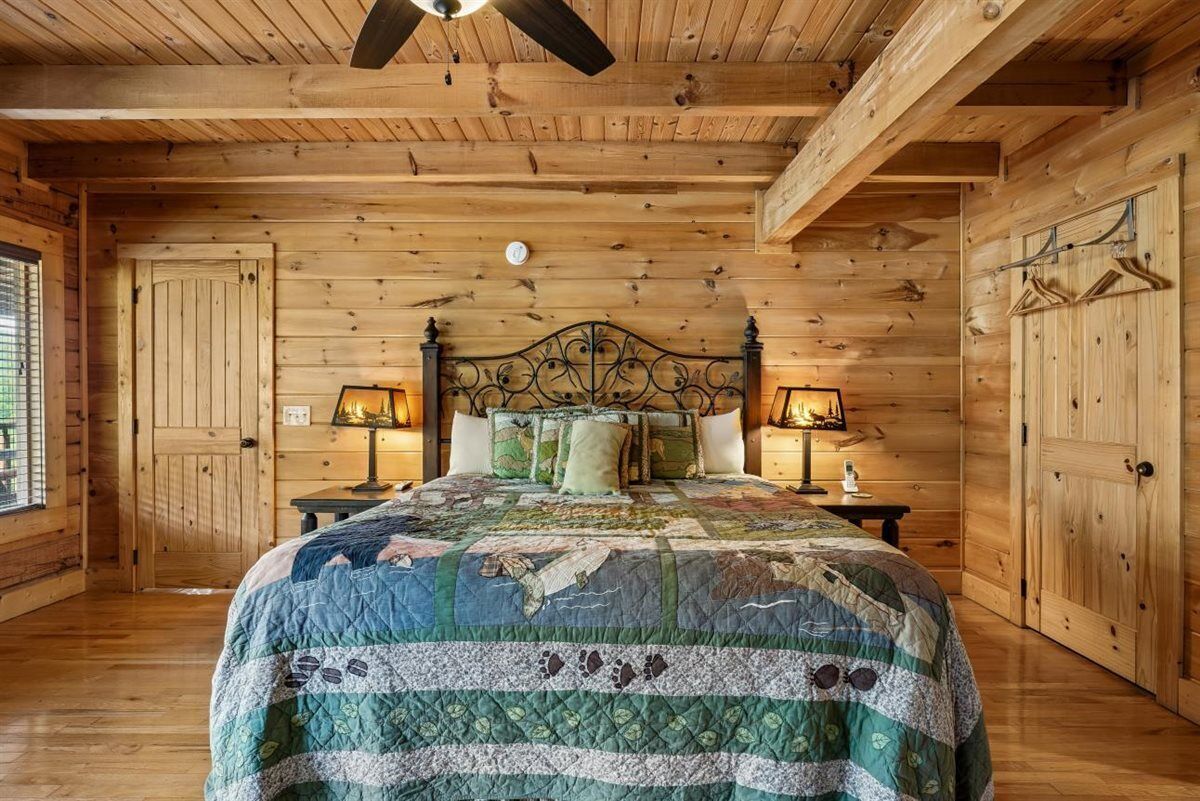 Een houten slaapkamer met een bed, twee nachtkastjes, een plafondventilator en houten wanden.