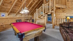 Un interior de madera con una mesa de billar, un sofá y una escalera.