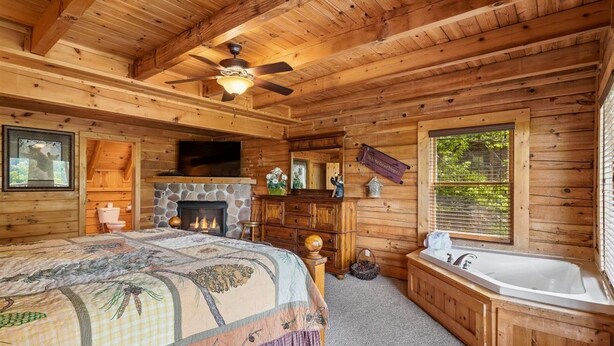 Un dormitorio de cabaña de troncos con cama, chimenea, ventana grande y bañera.