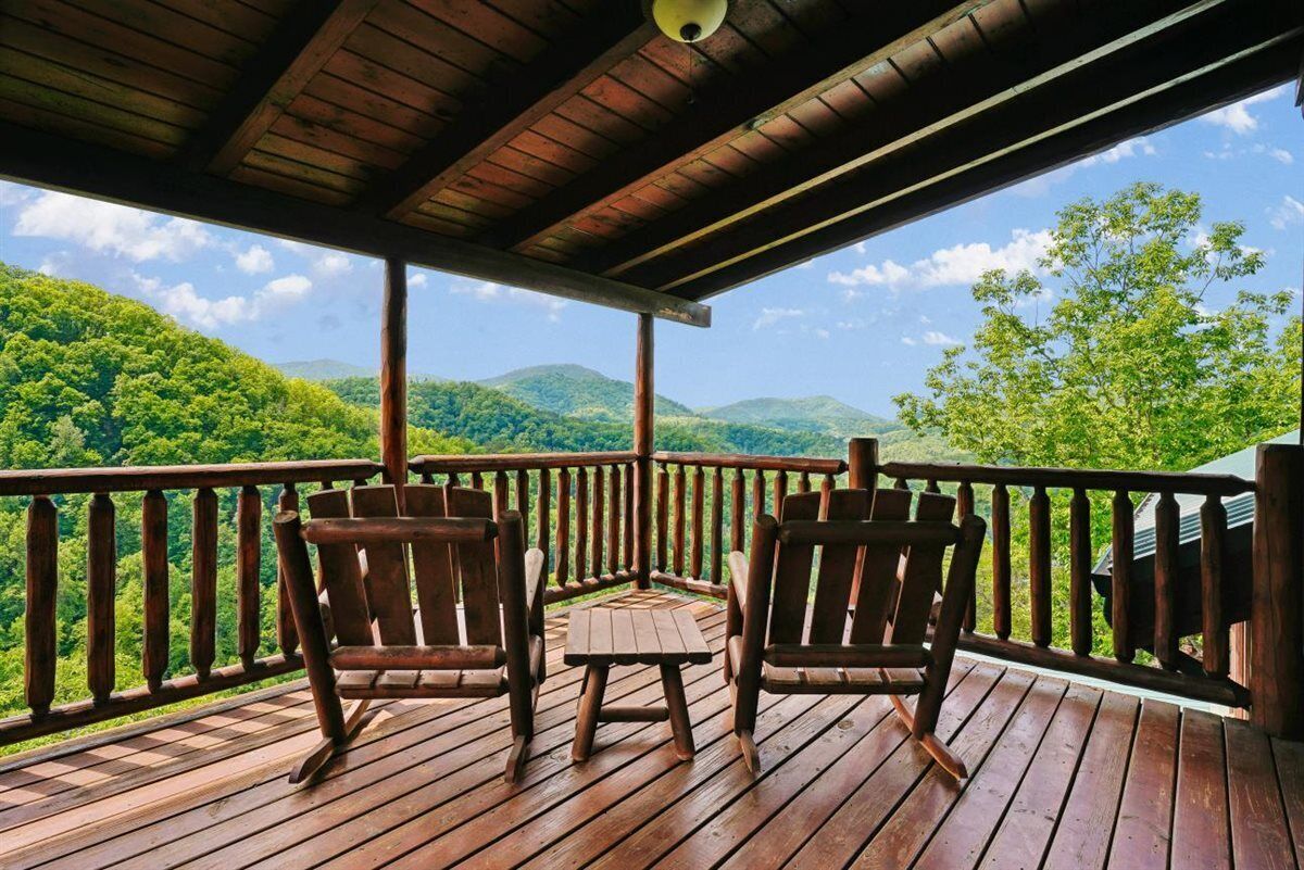 A wooden deck with two rocking chairs and a small table, overlooking a forested landscape.