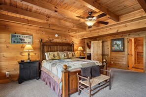 A wooden cabin interior with a bed, two nightstands, a chair, a ceiling fan, and a sign reading 'Bear Creek Lodge'.