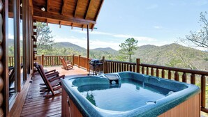 A wooden deck with a hot tub, wooden chairs, and a view of mountains.