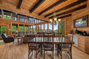 A spacious wooden interior with a dining area, seating, and large windows. - 7-Bedroom Cabin with Game Room & Hot Tub (Sevierville)