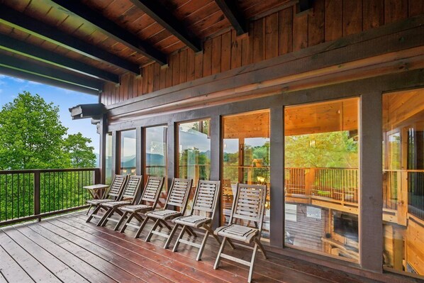 A wooden deck with lounge chairs and large windows overlooking a green landscape.
