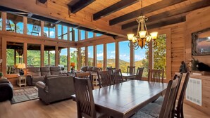 Amplia sala de estar con un gran comedor de madera, asientos cómodos y ventanas amplias con vistas al exterior.