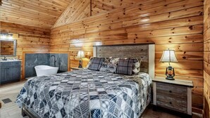 Ein Schlafzimmer einer Holzhütte mit Bett, Nachttischlampen, einem Waschbecken und einer Badewanne.