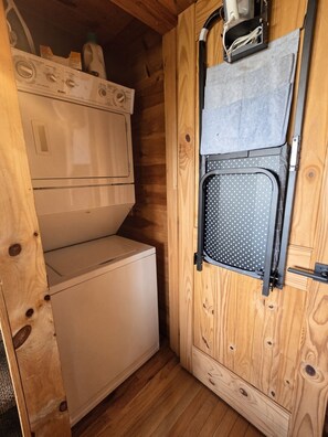 Una habitación pequeña de madera con lavadora, tendedero y un mueble bajo.