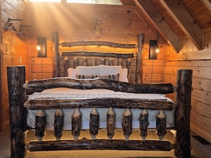 A log cabin bedroom with a bed made of logs, a deer head mounted on the wall, and two wall-mounted lights.