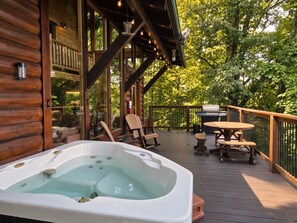 Eine Holzterrasse mit Whirlpool, Sitzgelegenheiten im Freien und einem Grill.