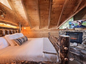 Ein gemütliches Blockhauszimmer mit Bett, Kamin und Fernseher.