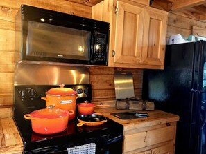 A kitchen with wooden cabinets, a black stove, a microwave, and a refrigerator.