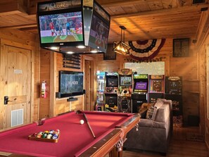 A wooden interior with a pool table, a television, and various arcade games.