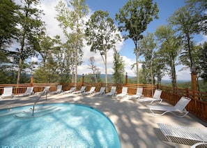 A pool area with lounge chairs and a wooden deck overlooking a forested landscape.