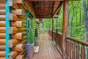 A log cabin with a wooden porch, a welcome mat, and potted plants.