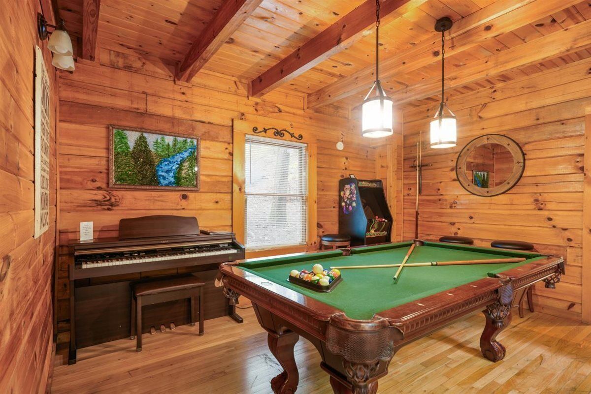 A wooden interior with a pool table, a piano, and a painting.