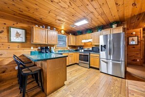 Cocina de cabaña de madera con una isla central, electrodomésticos de acero inoxidable y armarios de madera.