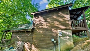 A wooden cabin with a balcony, surrounded by trees. - Cozy Rustic Cabin w/ Hot Tub & Pool Table (Sevierville)