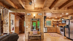 A wooden cabin interior with a kitchen, dining area, and a staircase leading to an upper level. - Tranquil Views w/ Mountain Views & Hot Tub (Sevierville)