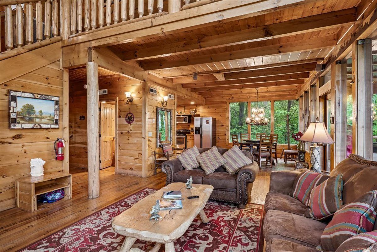 A log cabin interior with a wooden dining area, a sofa, and a television mounted on the wall.