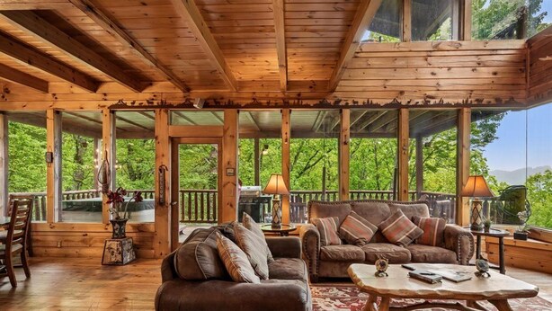 A wooden cabin interior with a large window, a sofa, a coffee table, and a dining area. - Tranquil Views w/ Mountain Views & Hot Tub (Sevierville)