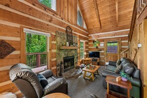 A log cabin interior with a fireplace, leather sofas, a television, and a stone accent wall.