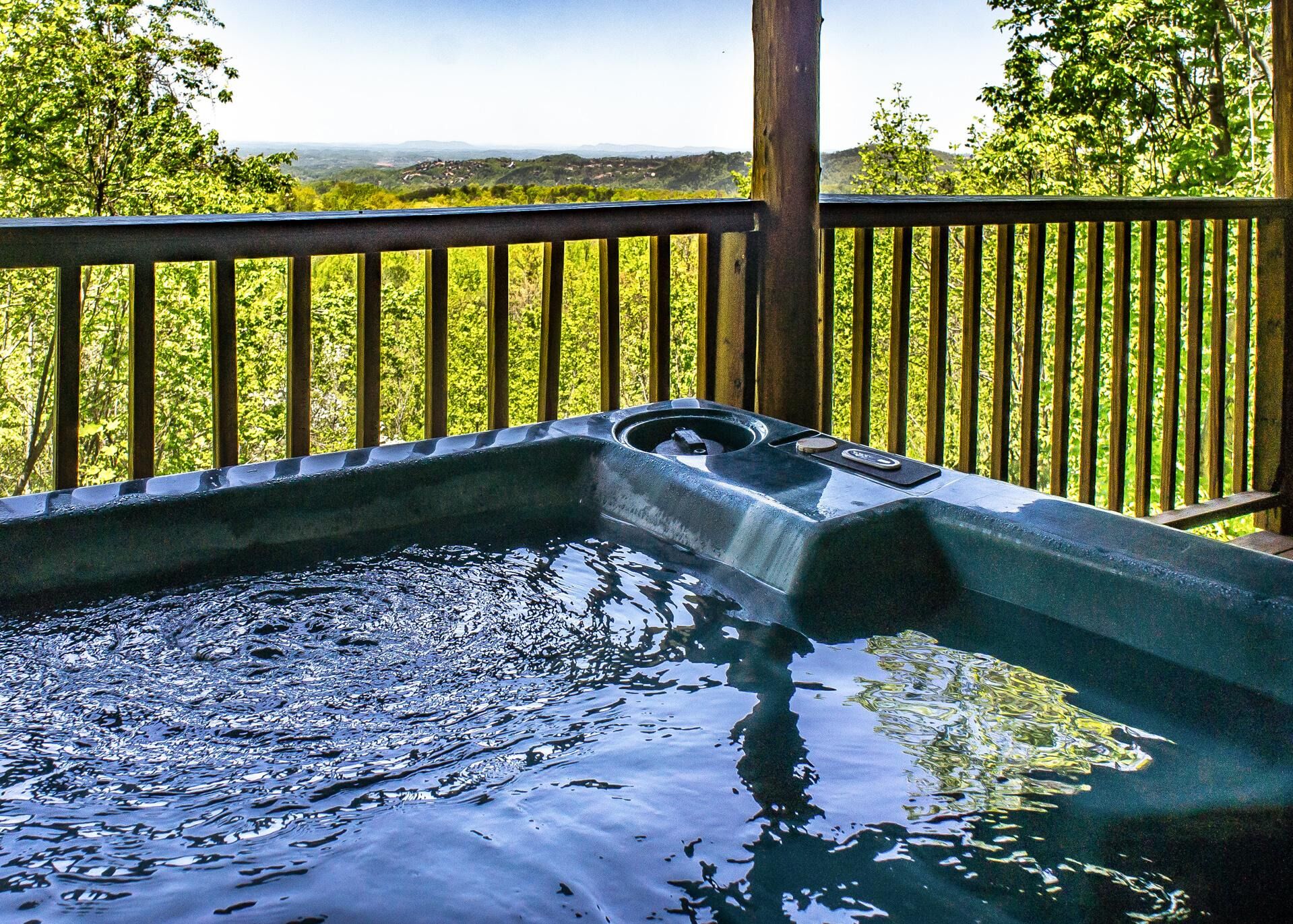 A hot tub with a wooden deck and a scenic view of hills and trees.